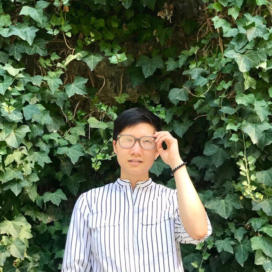 Photo of Karen Zheng by Ray Ren (Poet with short hair and brown-rimmed glasses, wearing a black-and-white striped buttoned shirt and standing in front of a background of ivy)
